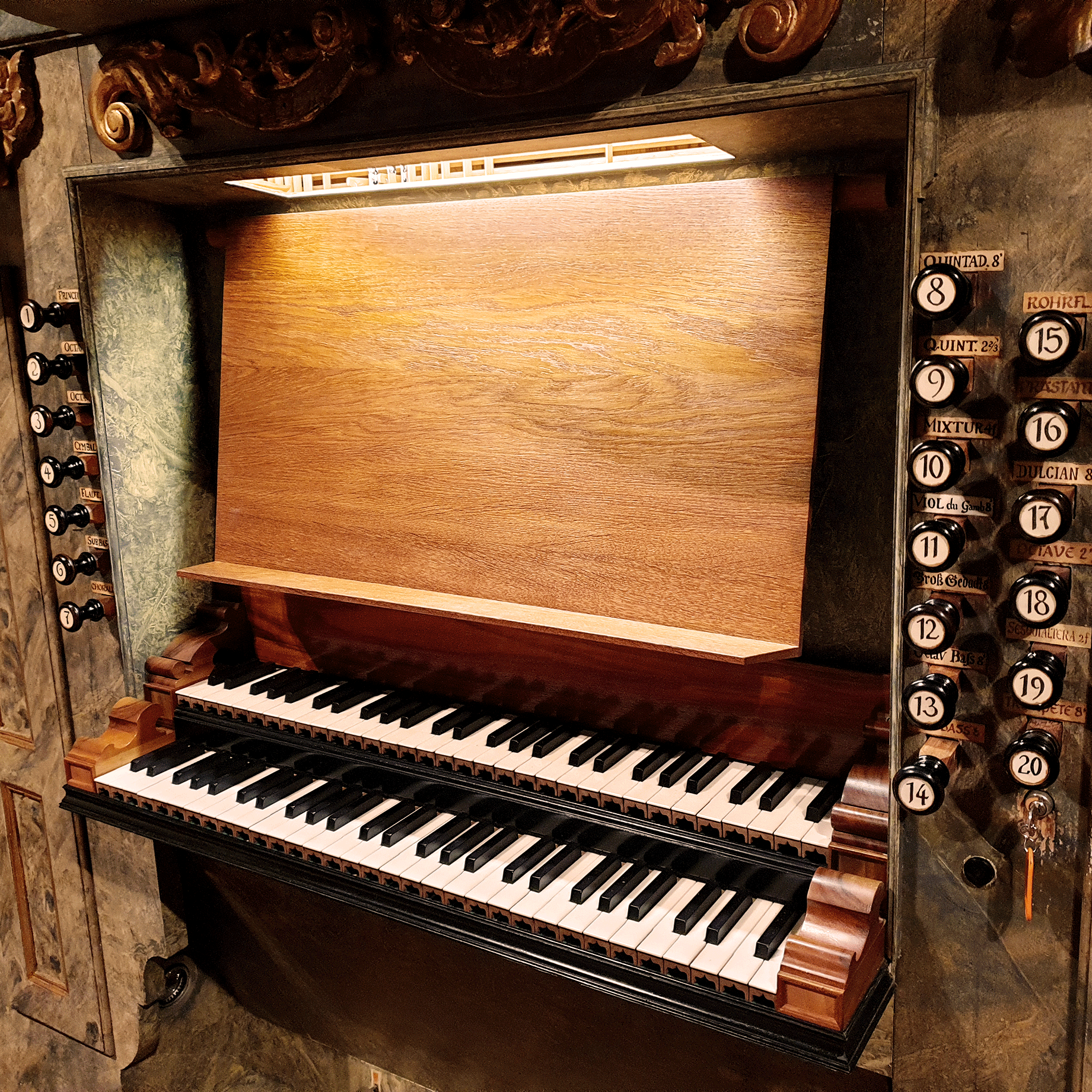Notenhalter-aus-Holz-an-orgel Manuale und Registerzüge einer historischen Kirchenorgel mit hölzernem Spieltisch und barocken Verzierungen.