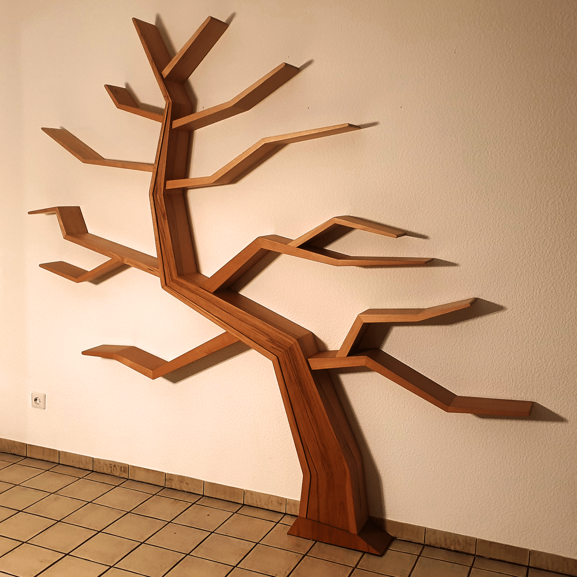 komplexes-Holzregal-in-Baumoptik-final-montiert Wandregal aus Holz in Form eines Baumes mit kantigen Ästen, montiert an einer hellen Wand. Bodenfliesen sorgen für eine kontrastierende Textur.